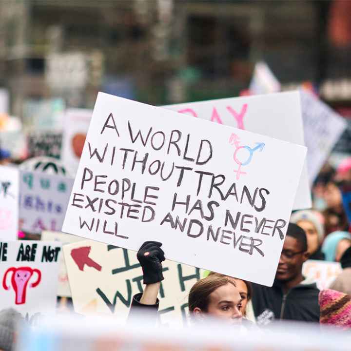 A pesron holding up a sign reading "A World Without Trans People Has Never Existed And Never Will" at a demonstration.