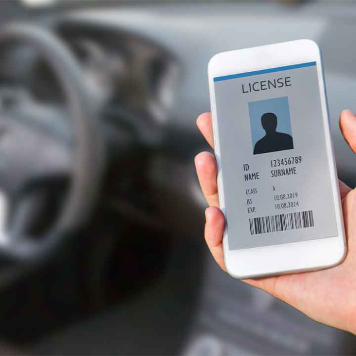 A hand (within a car) holding a cellphone displaying a digital drivers license.